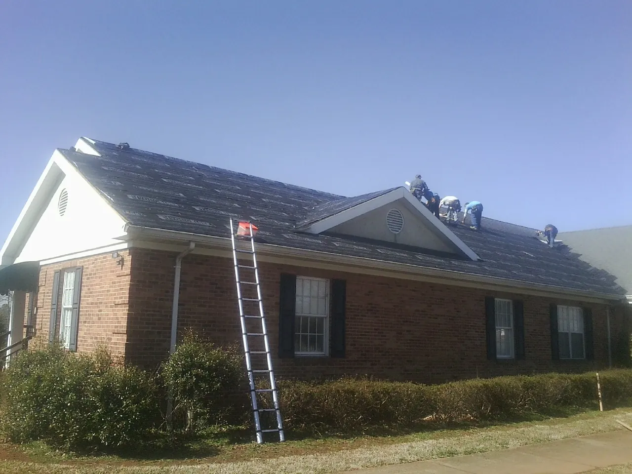 Crew tearing shingles off a brick ranch roof with a ladder set — Metal Roof Repair work by our crew in Rome City