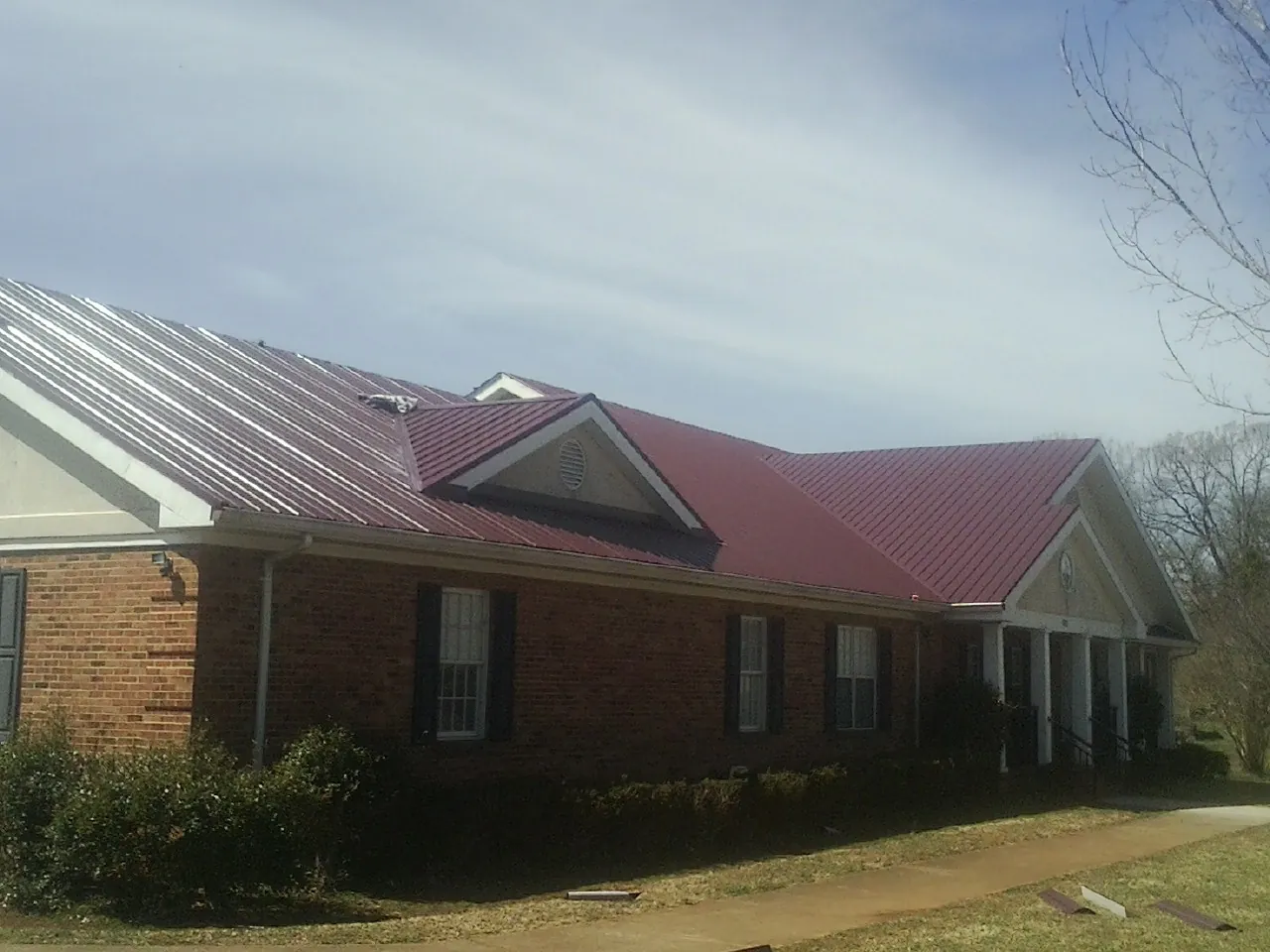 Red metal roof with gabled entries on a long brick building, from a Hail Damage Roof Repair job in Rome City