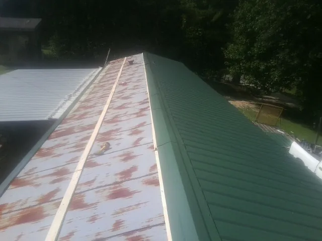 Old rusted panels beside newly installed green metal roofing — Wind Damage Roof Repair by Roofing Brothers in Rome City
