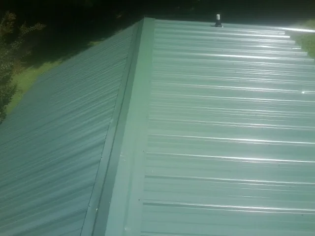 New green metal panels meeting at the ridge of a roof — Flat Roof Repair work by our crew in Rome City