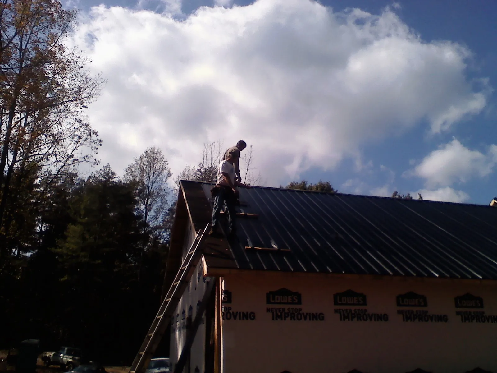 Roofer fastening dark metal panels high against a cloudy sky, from a Roof Inspection job in Rome City