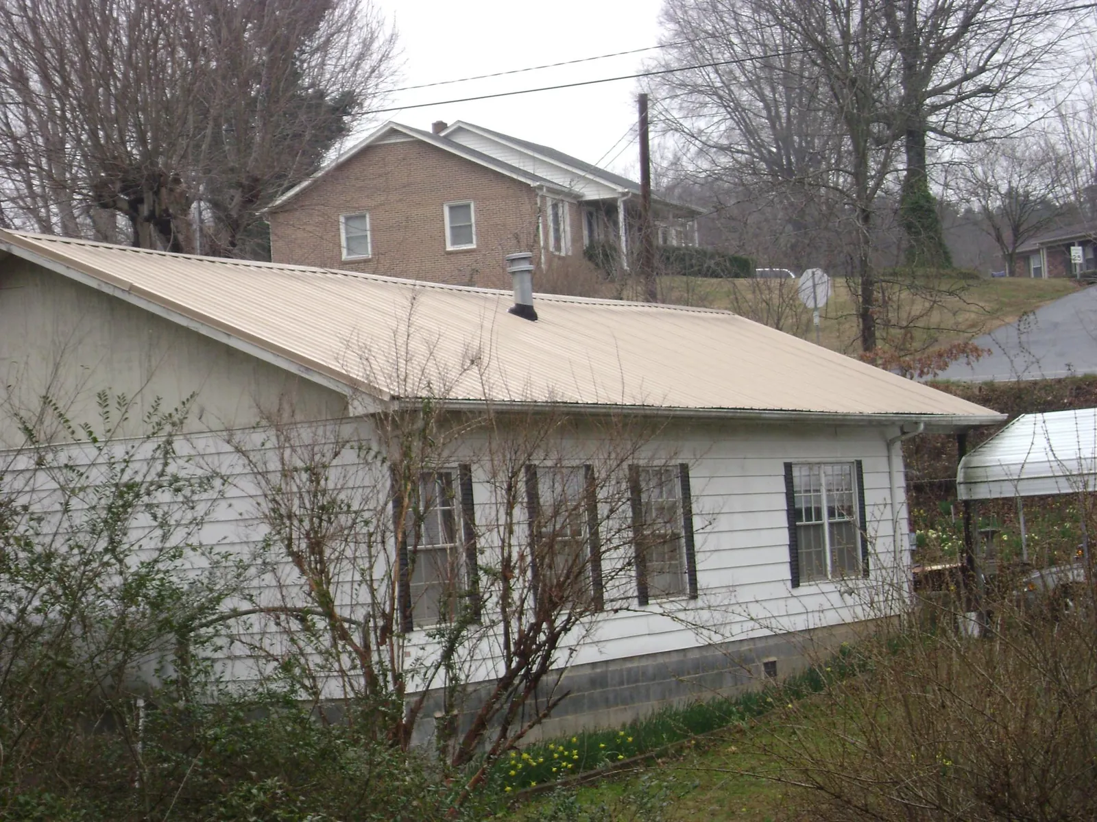 Tan metal roof on a white sided house set into a hillside — Commercial Roofing by Roofing Brothers in Rome City