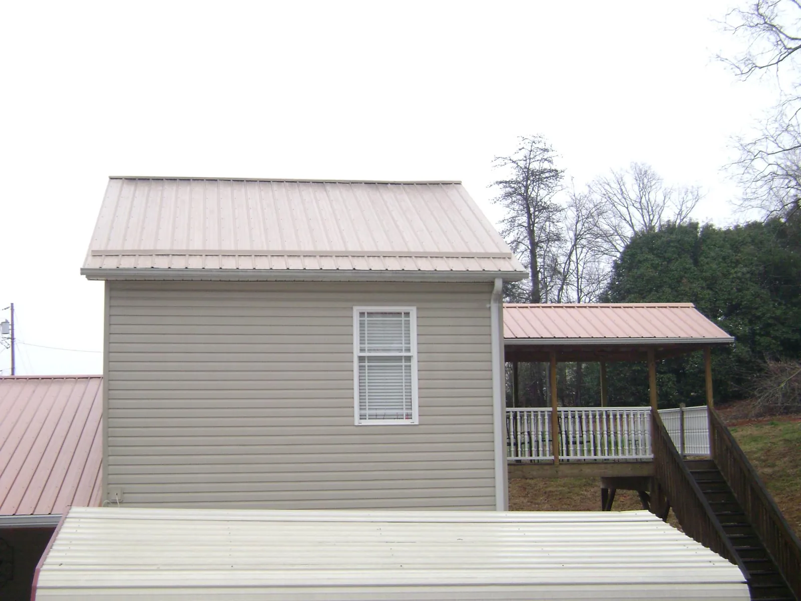 Tan metal roofs on a two story addition and attached porch, from a Roof Replacement job in Rome City